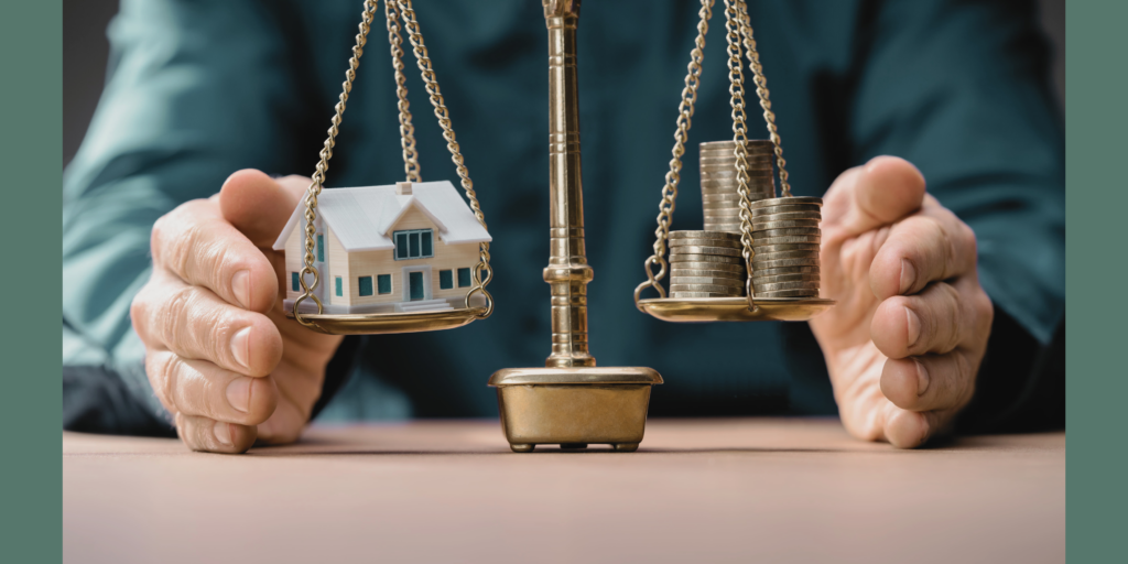 Golden scales sit on a table in front of a man. His hands are on either side of the scales shielding them. One side holds a small model of a home, while the other side is stacked with coins. They are in perfect balance.